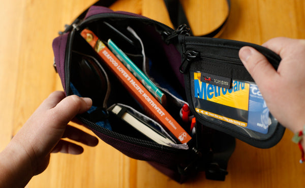 A person retrieving their clipped-in wallet from the main pocket of the Side Kick.